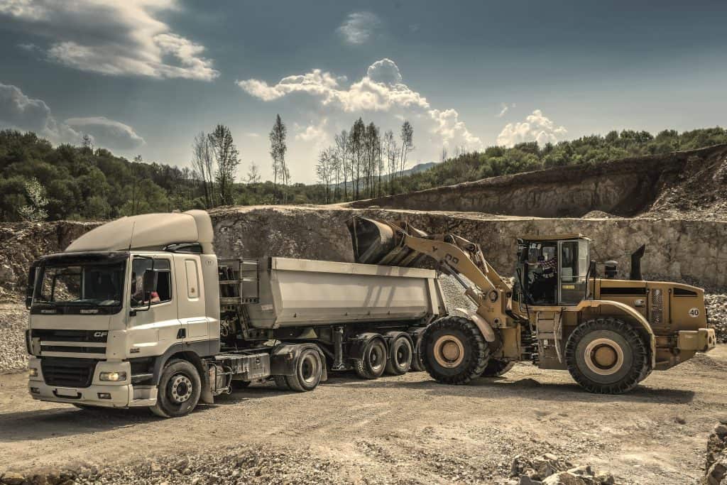 An auto dump truck is parked in front of a quarry.
