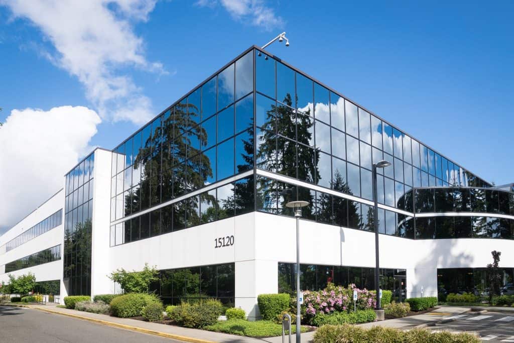 A commercial office building featuring glass windows and trees.