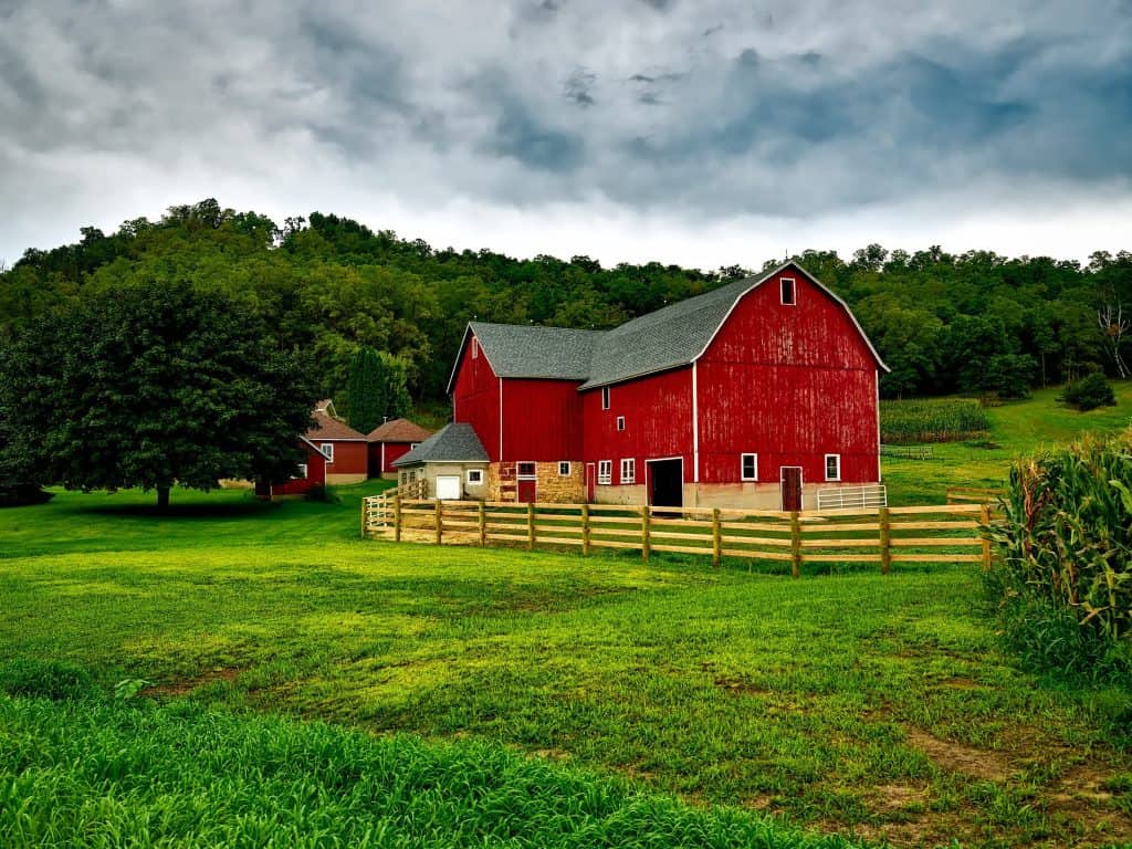 A red barn sits in a farm field under a stormy sky.