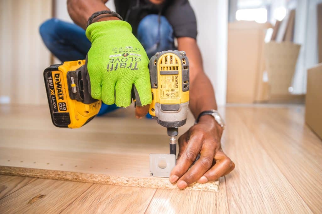 A man using a drill on wood flooring for General Liability purposes.