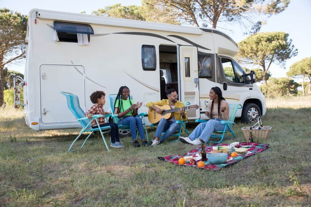 A group of people playing guitar in front of an RV.