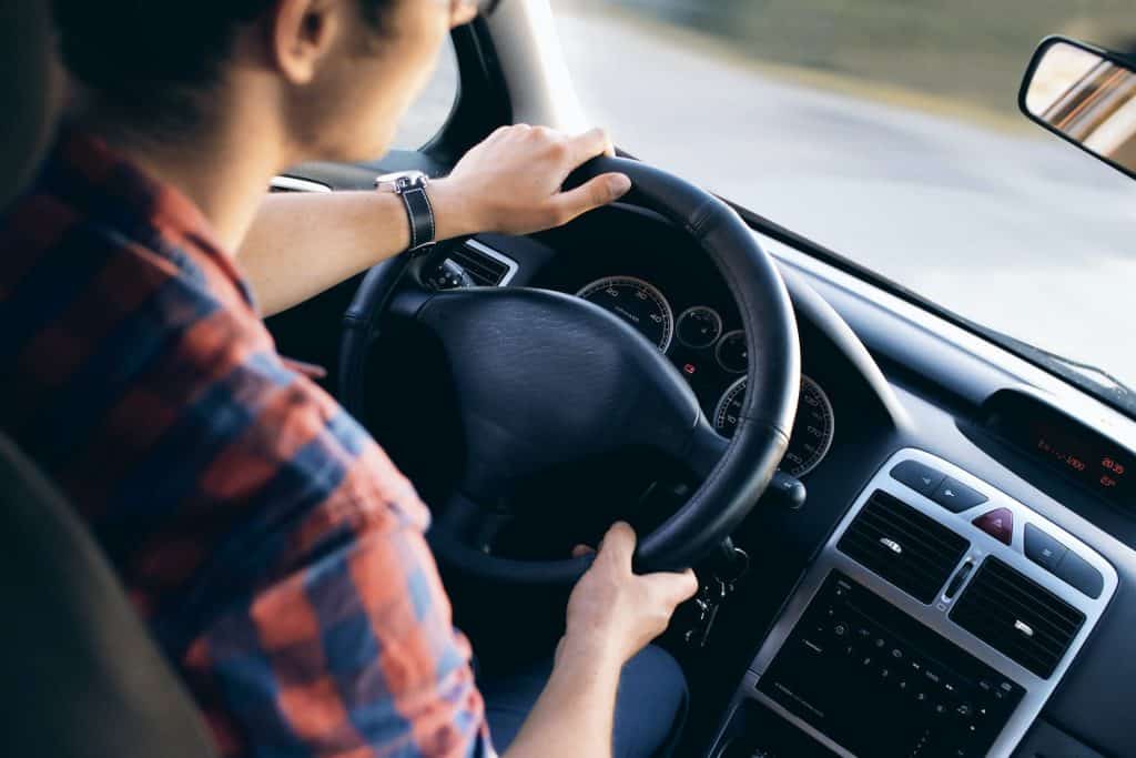 A man driving an auto with his hands on the steering wheel.