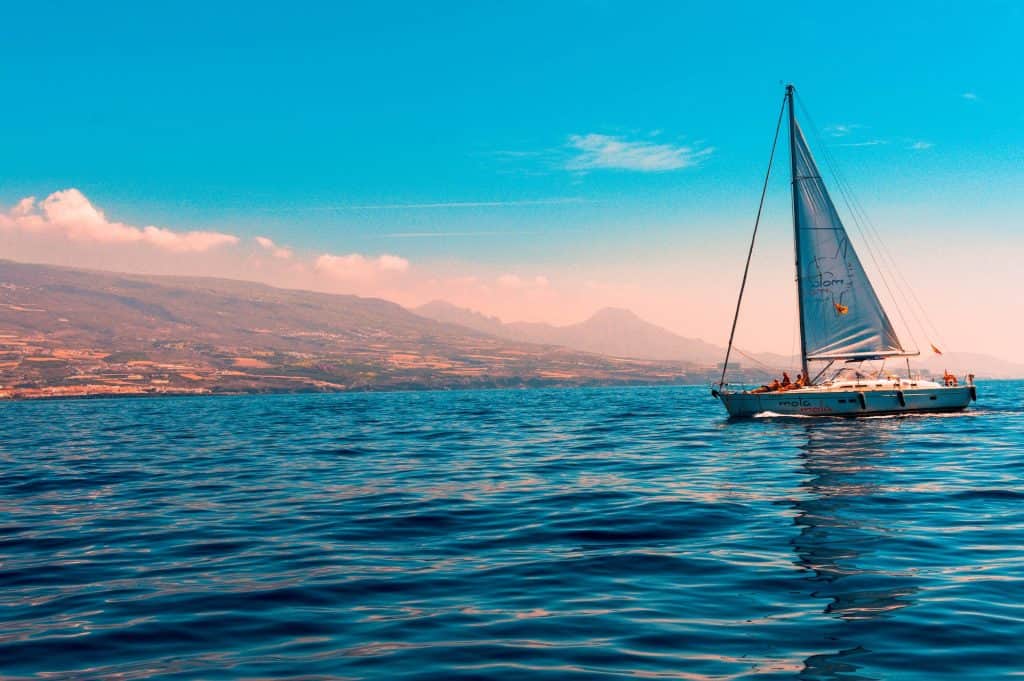 A boat sailing in the ocean with mountains in the background.