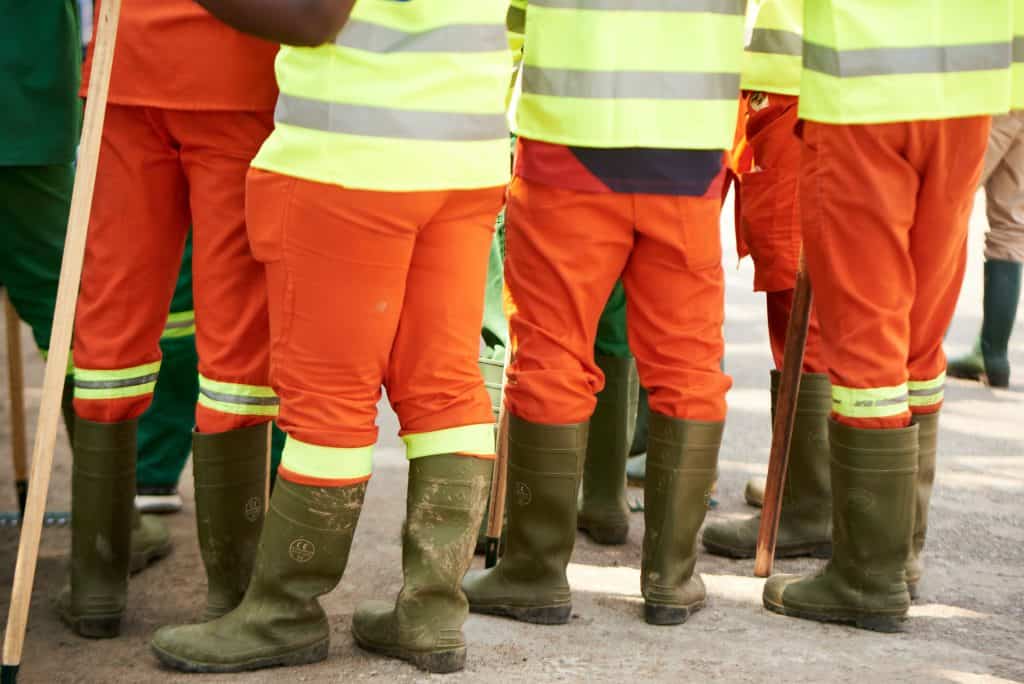 A group of workers wearing orange vests and green boots.